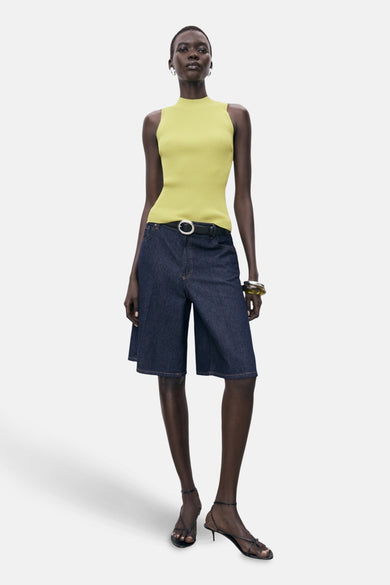 T-shirt jaune de MANGO, avec une texture à fines rayures, porté avec des bermudas en denim et des baskets.