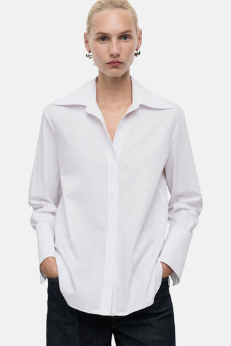 Blouse blanche à manches longues de MANGO, avec une encolure large et des jeans bleus foncés.