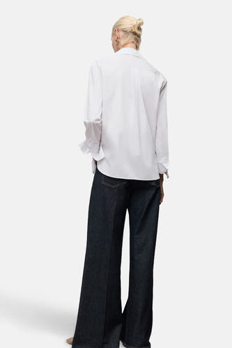 Blouse blanche à manches longues de MANGO, portée avec des jeans bleus marine à larges bords.