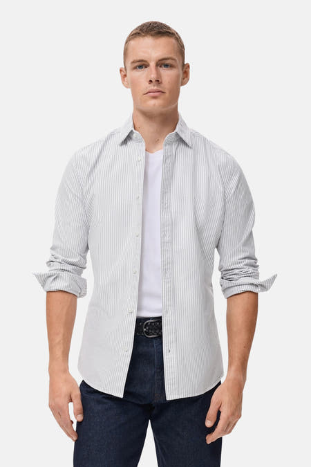Chemise rayée à manches longues de MANGO portée sur un T-shirt blanc et des jeans foncés avec une ceinture.