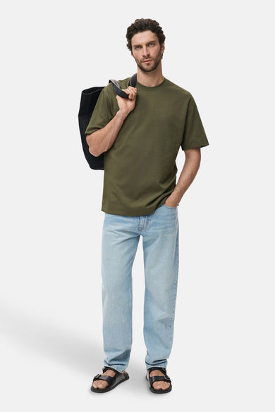 T-shirt kaki à manches courtes de MANGO, avec une sacoche noire sur l'épaule et des jeans légers.
