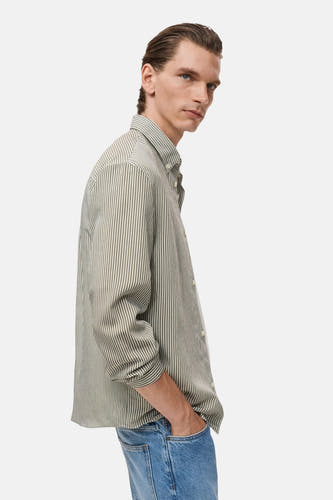 Chemise rayée kaki de MANGO à manches longues, portée avec un jean bleu, vue latérale.