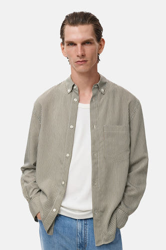 Chemise kaki à manches longues de MANGO, à rayures et avec une poche poitrine port port port sur sur un-shirt blanc.