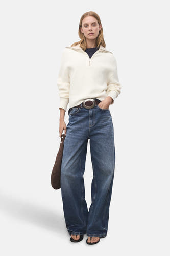 Pull-over blanc avec col montant de MANGO, porté avec des jeans larges, une ceinture marron et des sandales.