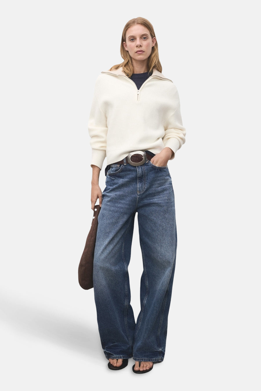 Pull-over blanc avec col montant de MANGO, porté avec des jeans larges, une ceinture marron et des sandales.