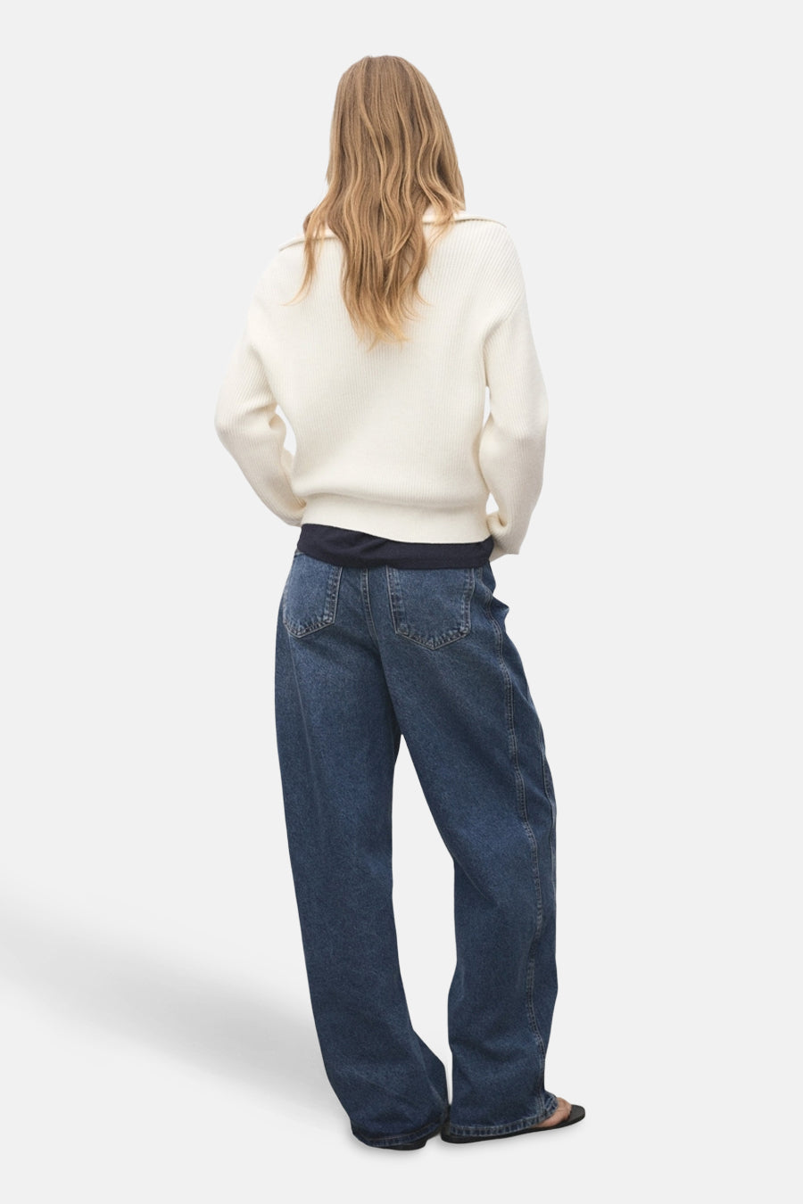 T-shirt à col rond blanc de MANGO, avec des manches longues, associé à des jeans larges et des sandales noires, vu de dos.