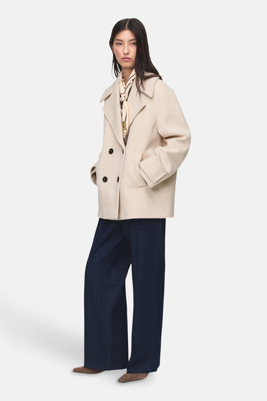 Manteau court beige de MANGO, avec une fermeture à double bouton et des poches, associé à un foulard en soie et à des jeans larges bleu marine.