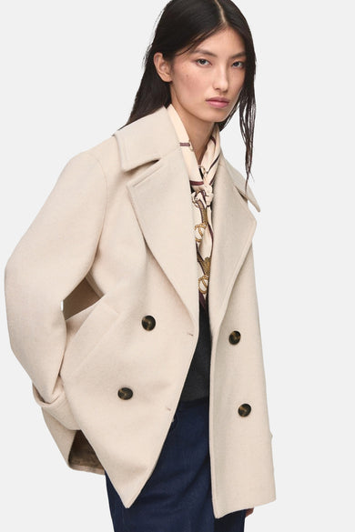 Manteau court beige de MANGO, avec des boutons doubles et un collier à motif chaîne.