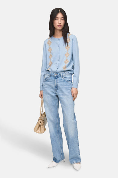 Gilet bleu de MANGO, avec un motif argyle sur l'avant, associé à des jeans larges et des escarpins blancs.