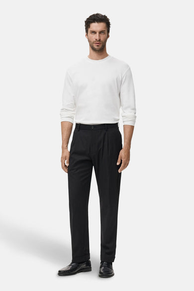 T-shirt blanc à manches longues de MANGO, porté avec un pantalon noir plié et des bottines en cuir.