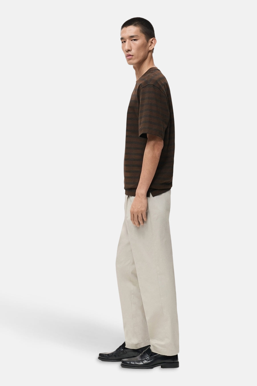 Man met bruin gestreept shirt, beige broek en zwarte loafers.