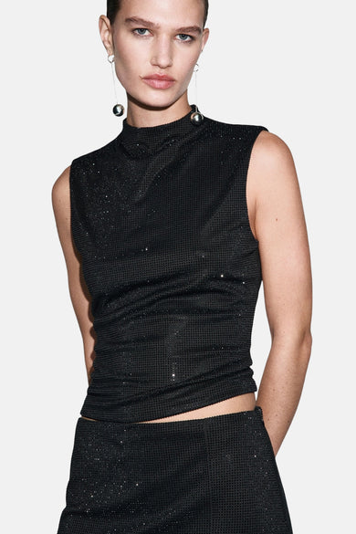 Vrouw in mouwloze zwarte glittertop en rok met zilveren oorbellen.
