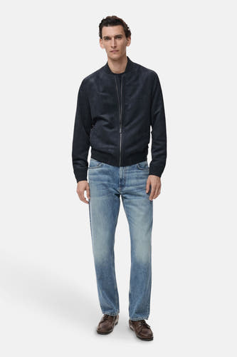 Manteau bleu court de MANGO, avec des manches longues et une fermeture éclair argentée, associé à un jean bleu et des chaussures marron.