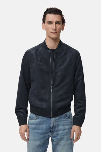 Manteau court bleu de MANGO, avec une fermeture éclair et porté sur un pantalon de cuir bleu.
