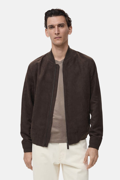 Manteau court brun de MANGO, avec fermeture éclair et longues manches, porté sur un T-shirt beige et des pantalons blancs.