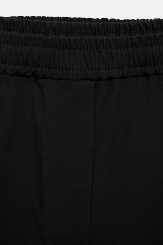 Pantalon noir de MANGO, avec une ceinture élastique et des fines coutures verticales.
