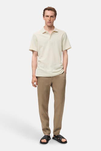 Polo écru à manches courtes de MANGO, porté avec un pantalon de lin marron et des sandales noires.