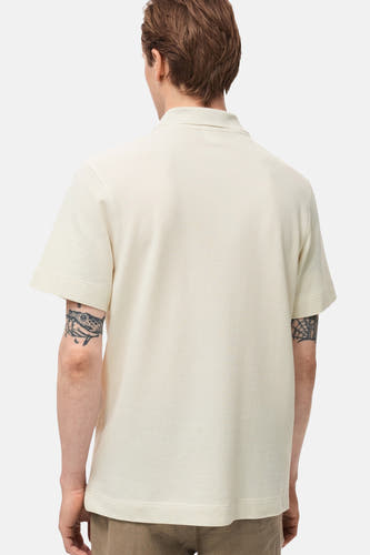 Polo écru à manches courtes de MANGO, vu de l'arrière, avec des tatouages sur les deux bras.