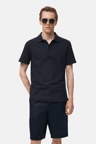 Polo bleu marine à manches courtes de MANGO, porté avec des shorts bleu marine et un casque.