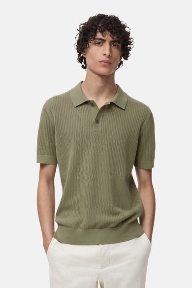 Kaki polo avec des manches courtes de MANGO, à une texture tricotée et porté avec un pantalon blanc.