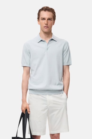 Polo bleu clair à manches courtes de MANGO, porté avec des shorts blancs et une sacoche noire.