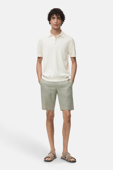 Polo écru à manches courtes de MANGO, porté avec des shorts en lin gris et des sandales brunes.