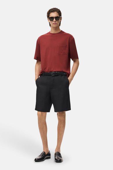 T-shirt rouge à manches courtes de MANGO, avec poche poitrine, porté avec des short noirs et des loafers.