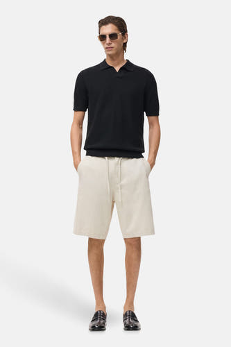 Jean écru court de MANGO, associé à un t-shirt polo noir, des lunettes de soleil et des loafers en cuir.