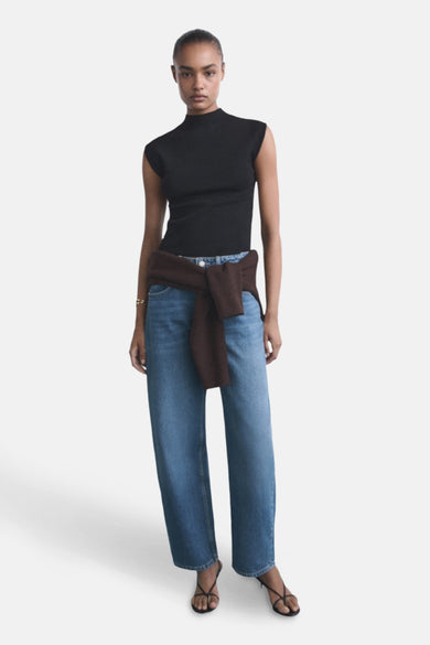 Jean en denim bleu marine de MANGO, avec des jambes larges et une chemise brune attachée nonchalamment autour de la taille.