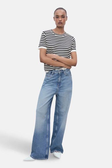 T-shirt multicolore à manches courtes de MANGO, avec des rayures horizontales, associé à des jeans larges et des chaussures blanches.
