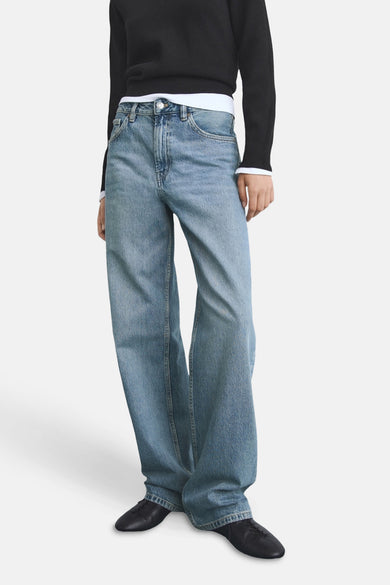 Jean en denim bleu droit de MANGO, porté avec un pull noir et des chaussures noires.