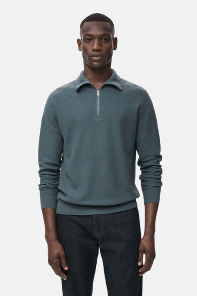 T-shirt bleu à col montant de MANGO, avec une fermeture éclair et porté avec des jeans foncés.