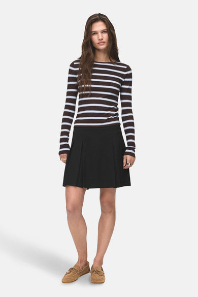Jupe courte noire de MANGO, associée à une chemise rayée et des chaussures en suède.