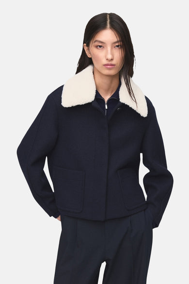 Manteau court bleu de MANGO, vu de de derrière, avec une collet bl et et un pantalon bleu marine.