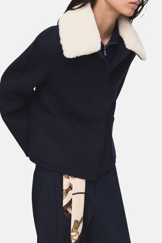 Manteau court bleu de MANGO, avec un col blanc et un foulard en soie comme accessoire.