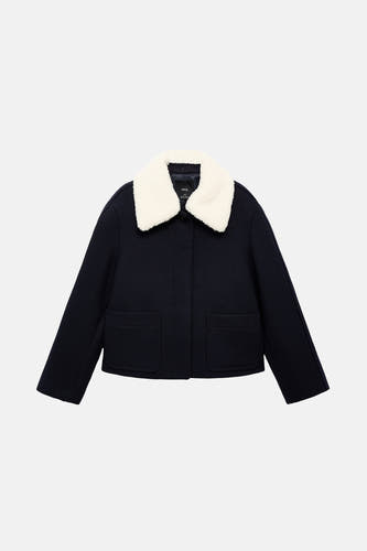 Manteau court bleu de MANGO, avec un col blanc en fourrure imitée et des poches brodées.