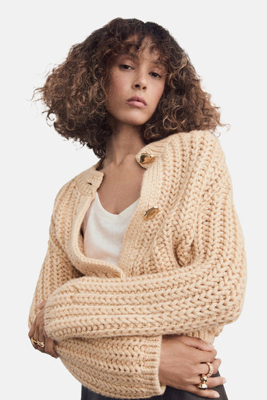 Gilet beige de MANGO, avec une structure en côtes grossières et une fermeture décorative dorée.
