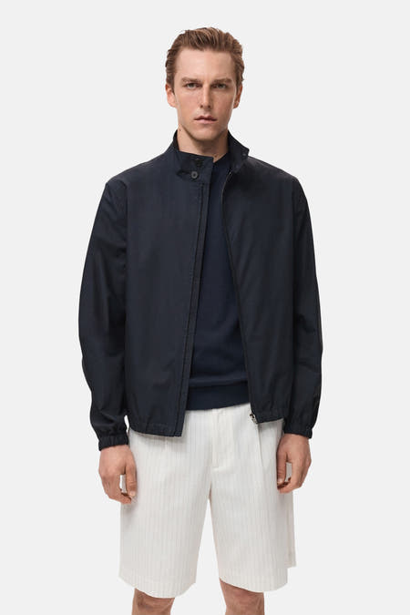Manteau court bleu de MANGO porté avec un pull bleu marine et des short rayés blancs.