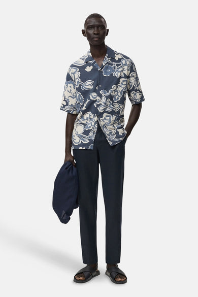 Pantalon bleu de MANGO, associé à une chemise à fleurs, des sandales et un sac.