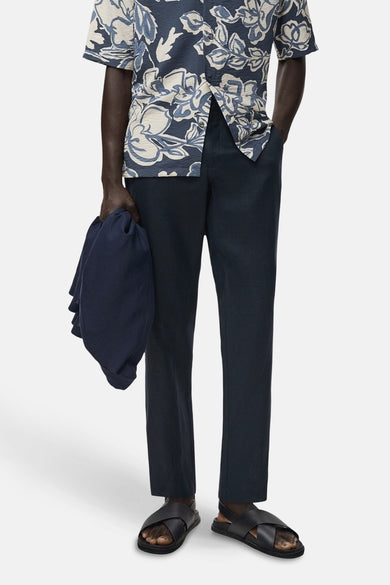 Pantalon bleu de MANGO, avec une texture lisse, associé à une chemise à imprimé floral et des sandales noires.