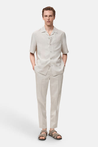 Pantalon écru de MANGO, porté avec un chemisier à manches courtes et des sandales en cuir.