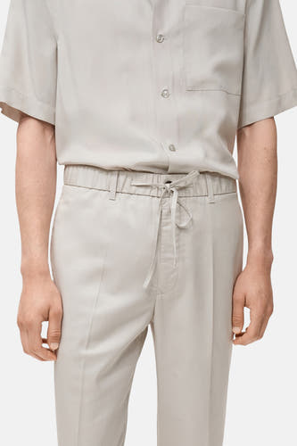 Pantalon écru de MANGO, avec cordon de serrage à la taille et un modèle légèrement cintré.