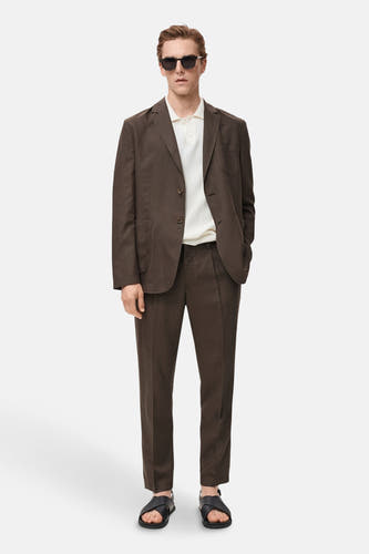 Blazer marron de MANGO, porté avec un polo blanc, un pantalon coordonné et des sandales noires.
