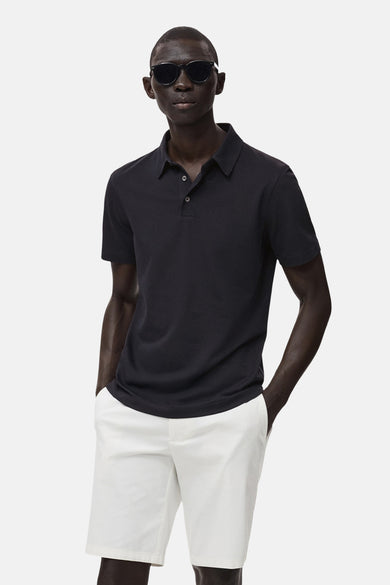 Polo bleu marine à manches courtes de MANGO, porté avec un short blanc et des lunettes de soleil.
