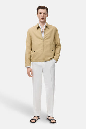 Manteau court beige de MANGO, porté avec un chemisier blanc, des pantalons blancs et des sandales noires.
