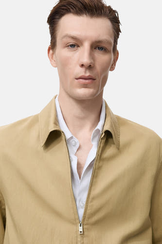Manteau court beige de MANGO, porté sur une chemise blanche à col ouvert.