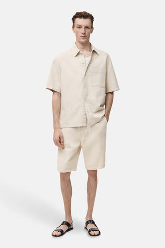 T-shirt en jeans en MANGO, couleur écru, avec des manches courtes et une poche à la poitrine, porté avec des shorts et des sandales coordonnés.