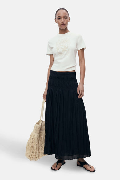 T-shirt écru à manches courtes de MANGO, avec un imprimé floral et associé à une longue jupe noire et un sac.
