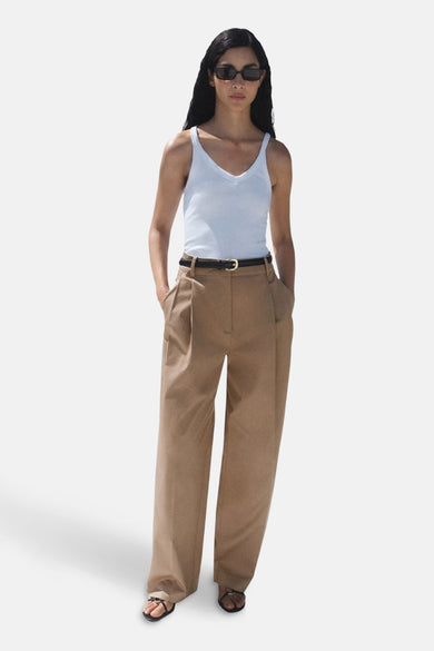 Pantalon beige de MANGO, avec plis, jambes larges, une ceinture noire et des sandales noires.