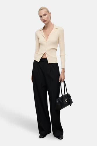 Cardigan jaune de MANGO, avec des manches longues, porté avec une jupe noire et un sac noir.